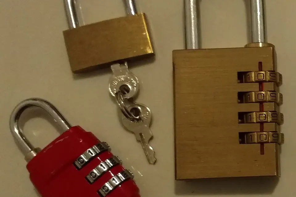 Three padlocks on a table: a brass key padlock, a brass combination lock and a small red combination lock