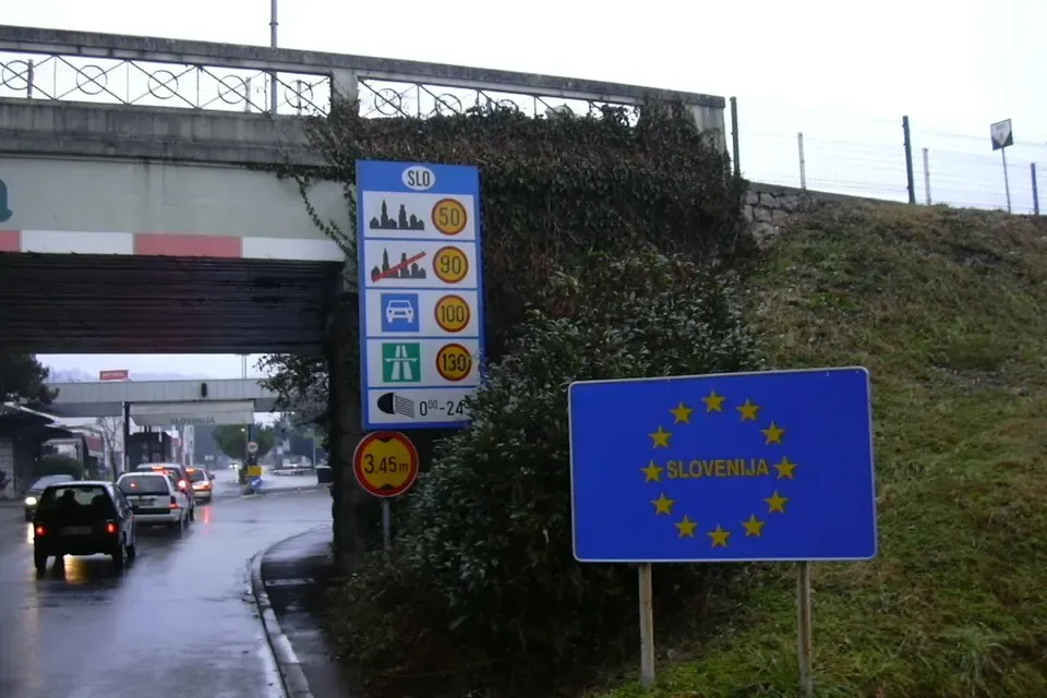 A blue European Union sign marking the Slovenian border beside a road that passes under a bridge
