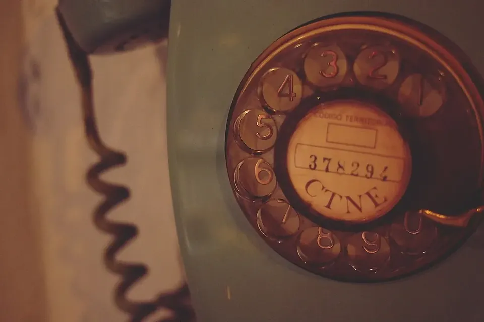 Close-up of an old rotary telephone dial with a paper number card at its centre and a coiled cord beside it