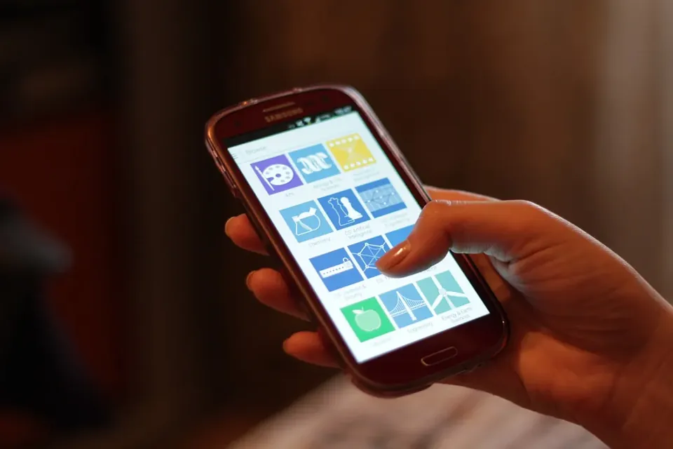A hand holding a smartphone whose screen shows a grid of colourful app icons