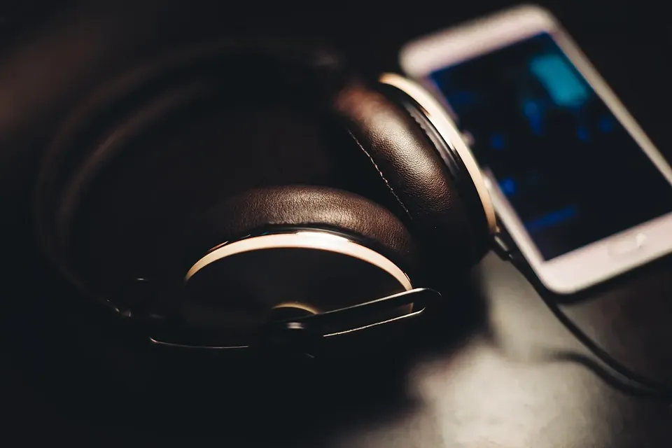 Over-ear headphones lying on a dark desk beside a smartphone with a lit screen