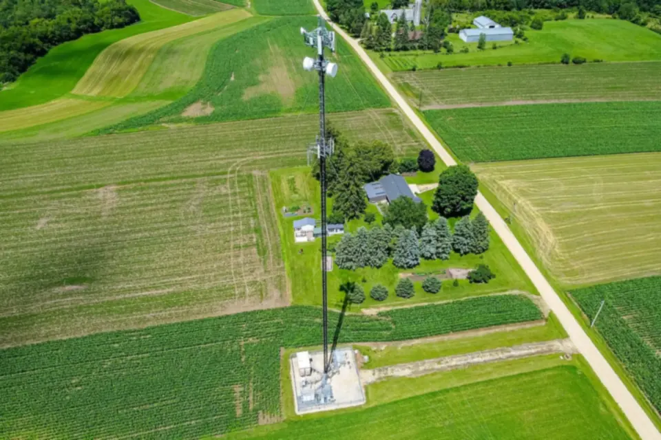 Aerial view of a lone mobile phone mast beside a country road, surrounded by green fields and a farmhouse