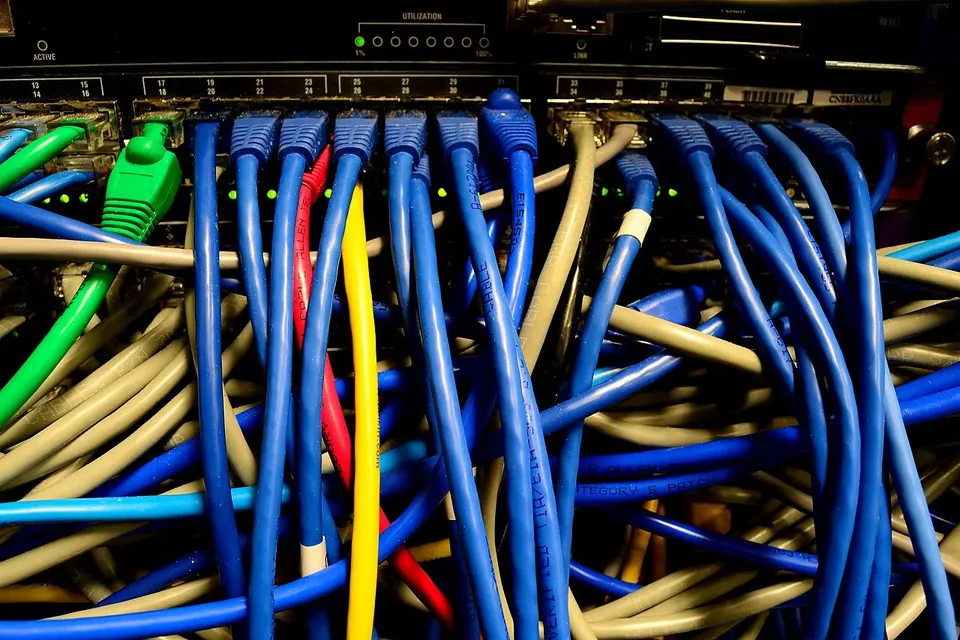 Dozens of blue, yellow and green network cables plugged into a rack-mounted Ethernet switch